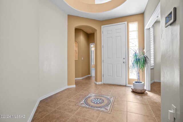 foyer entrance with light tile patterned floors, arched walkways, and baseboards