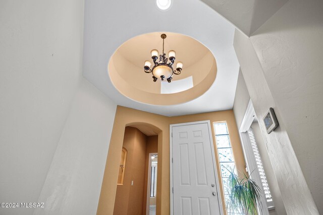 foyer entrance featuring an inviting chandelier, arched walkways, and a raised ceiling
