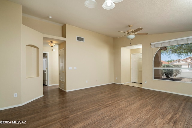 empty room with ceiling fan, vaulted ceiling, a textured ceiling, and dark wood-type flooring