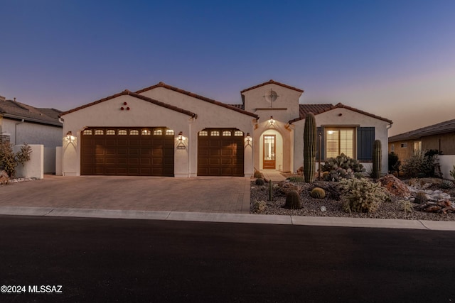 mediterranean / spanish home featuring a tiled roof, a garage, stucco siding, and driveway