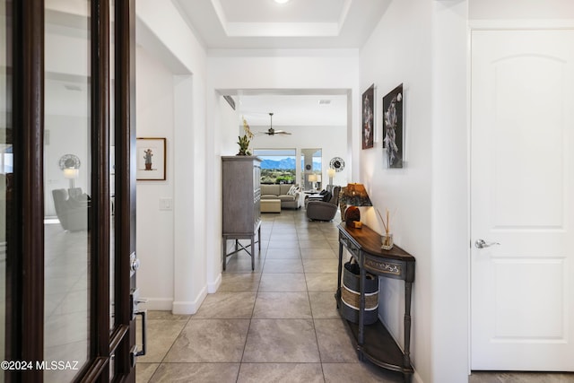 corridor with baseboards, light tile patterned floors, and a raised ceiling