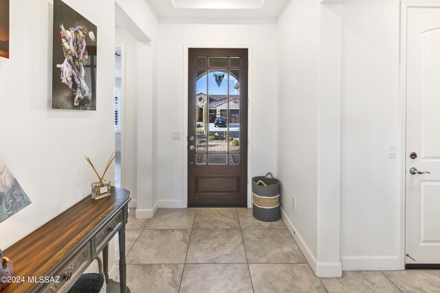 foyer entrance featuring baseboards, a tray ceiling, and light tile patterned flooring