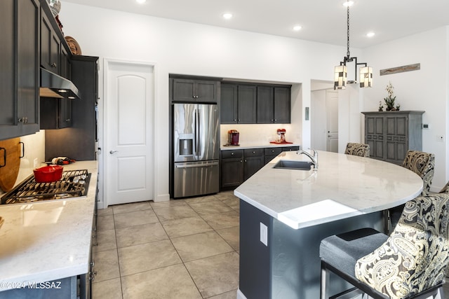 kitchen with light stone countertops, a breakfast bar area, under cabinet range hood, a sink, and appliances with stainless steel finishes