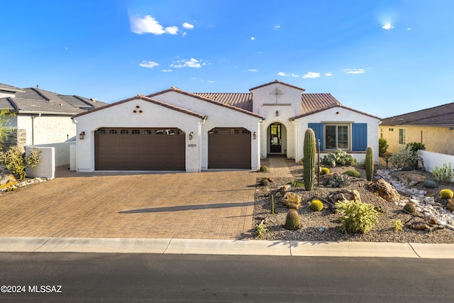 mediterranean / spanish house with decorative driveway, a garage, stucco siding, and a tiled roof