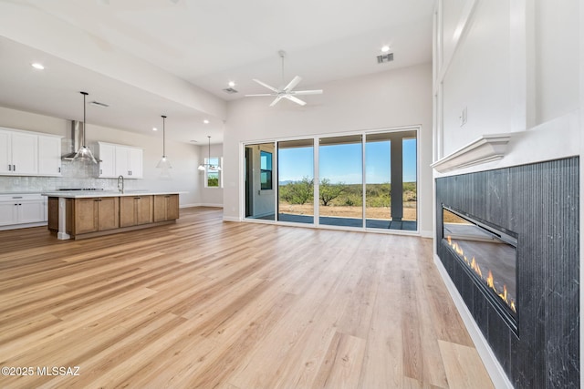 67970 E Madison Rd, Oracle, AZ 85623 - unfurnished living room with a glass covered fireplace, recessed lighting, ceiling fan, light wood-style floors, and a towering ceiling