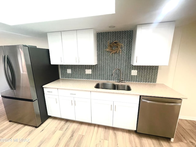 kitchen featuring backsplash, appliances with stainless steel finishes, white cabinetry, light wood-type flooring, and sink