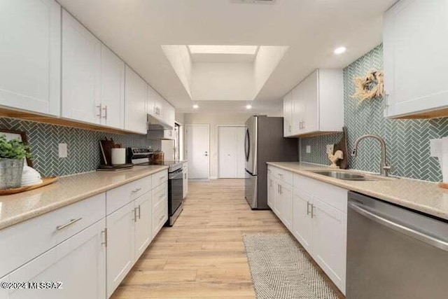 kitchen with appliances with stainless steel finishes, light hardwood / wood-style flooring, white cabinets, and tasteful backsplash