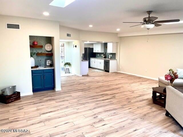 living room featuring ceiling fan, light wood-type flooring, and a skylight