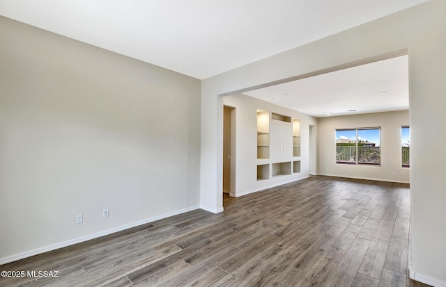 8257 S Silver Oak Dr, Tucson, AZ 85747 - unfurnished living room featuring dark wood-type flooring, baseboards, and built in features