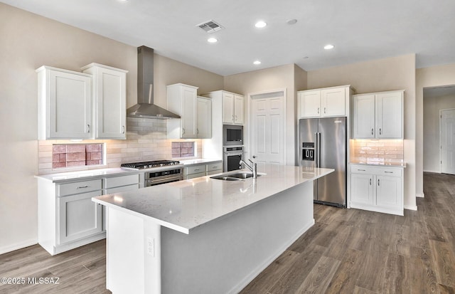 8257 S Silver Oak Dr, Tucson, AZ 85747 - kitchen with stainless steel appliances, wall chimney range hood, wood finished floors, a kitchen island with sink, and backsplash