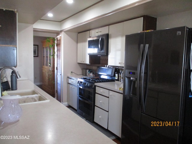 kitchen with white cabinets, sink, black fridge, and range with two ovens