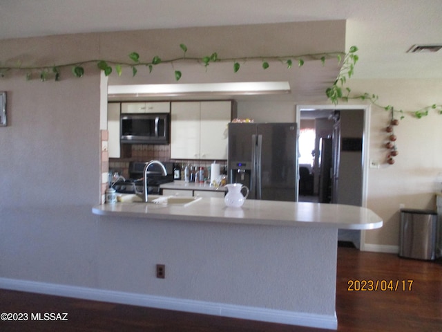 kitchen with stainless steel appliances, white cabinets, kitchen peninsula, and dark hardwood / wood-style flooring