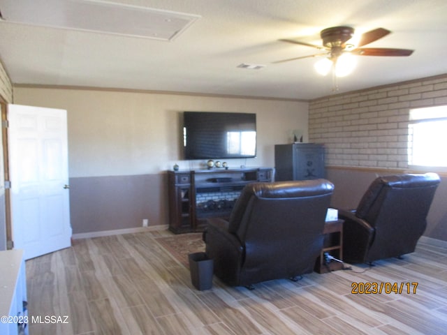 living room with light wood-type flooring, ornamental molding, ceiling fan, and brick wall