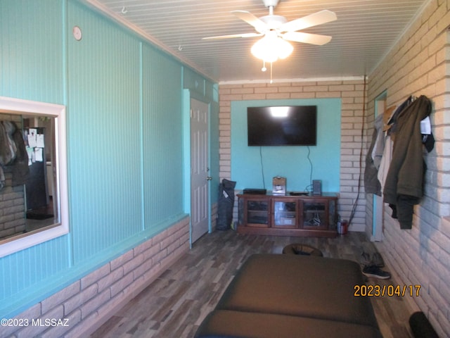 living room with wood-type flooring, ceiling fan, and brick wall