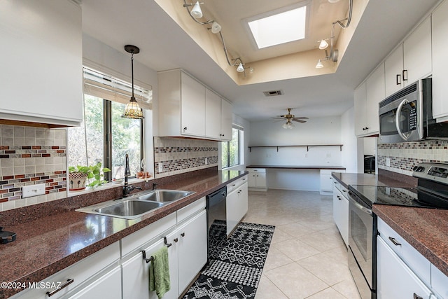 kitchen with stainless steel appliances, dark countertops, a raised ceiling, and a sink