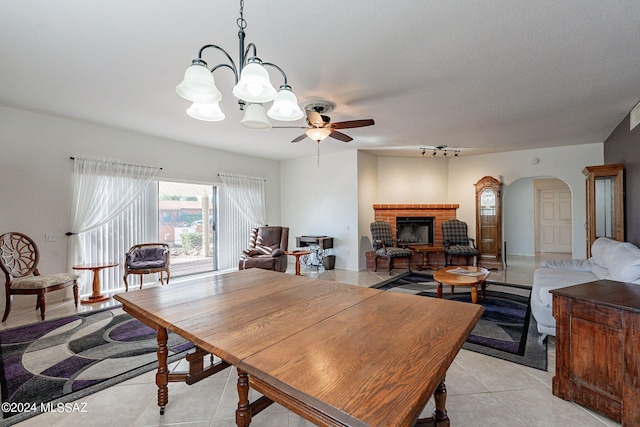 dining space with arched walkways, ceiling fan, a brick fireplace, and light tile patterned flooring