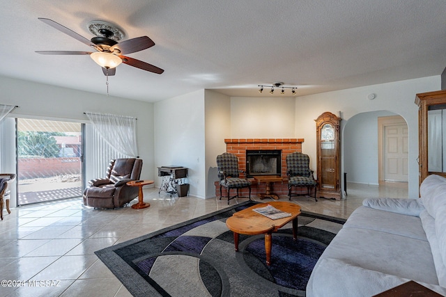 living room with arched walkways, a fireplace, light tile patterned floors, ceiling fan, and a textured ceiling