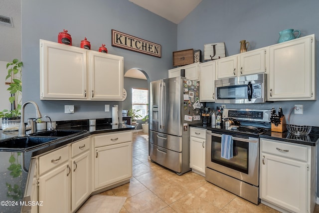 kitchen with white cabinets, light tile patterned floors, appliances with stainless steel finishes, high vaulted ceiling, and sink