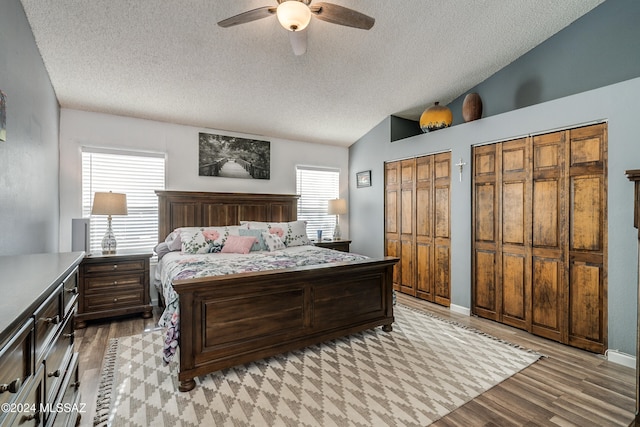 bedroom with light wood-type flooring, a textured ceiling, ceiling fan, vaulted ceiling, and two closets