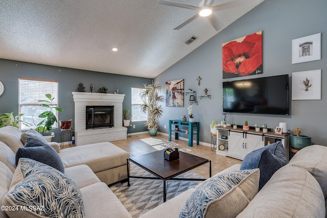 living room with vaulted ceiling, light tile patterned floors, a textured ceiling, a fireplace, and ceiling fan