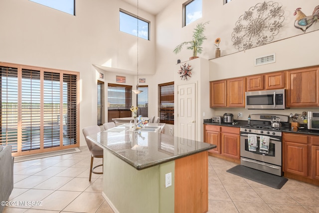 kitchen with hanging light fixtures, appliances with stainless steel finishes, a kitchen breakfast bar, a kitchen island with sink, and a high ceiling