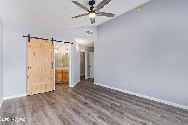 unfurnished bedroom with ceiling fan, a barn door, dark hardwood / wood-style floors, ensuite bath, and vaulted ceiling