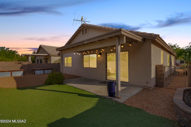 back house at dusk featuring a lawn and a patio area