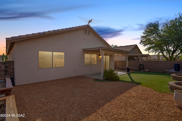 back house at dusk with a lawn and a patio area