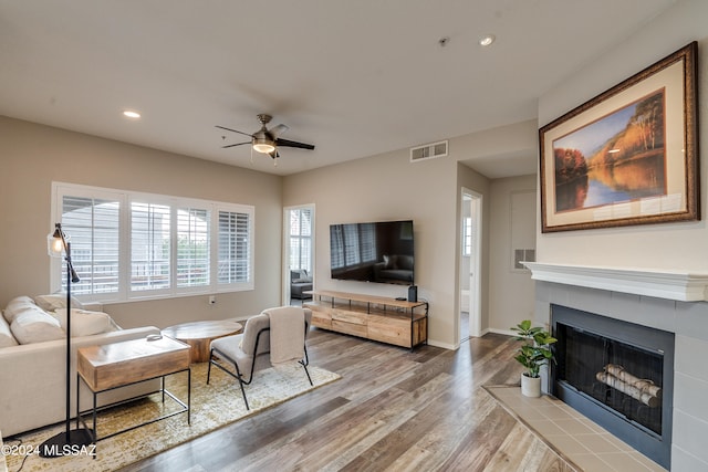 living room featuring wood-type flooring, ceiling fan, and a tile fireplace