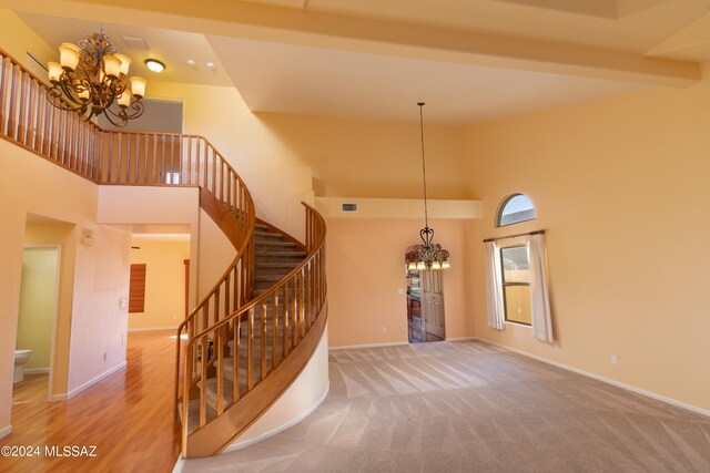 stairs featuring beam ceiling, a towering ceiling, carpet floors, and a chandelier