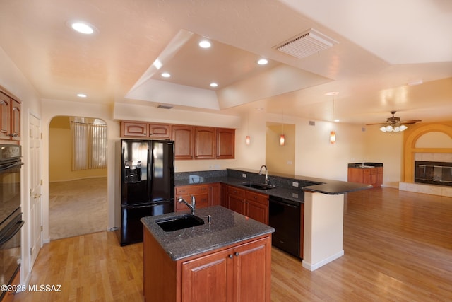 kitchen with a tiled fireplace, an island with sink, sink, and black appliances