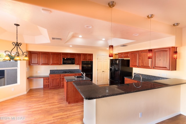 kitchen featuring hanging light fixtures, a tray ceiling, light hardwood / wood-style floors, black appliances, and kitchen peninsula