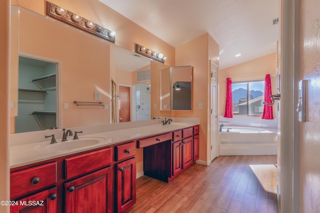 bathroom featuring vanity, hardwood / wood-style floors, lofted ceiling, and a tub to relax in