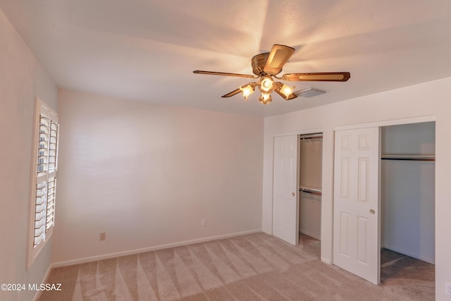 unfurnished bedroom with ceiling fan, light colored carpet, and two closets