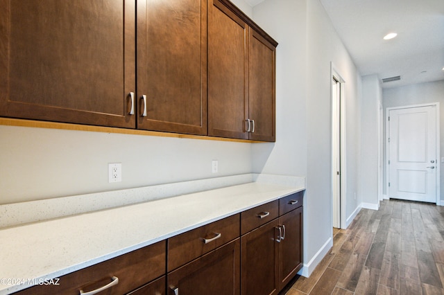 kitchen with dark wood-type flooring, light stone countertops, and dark brown cabinets