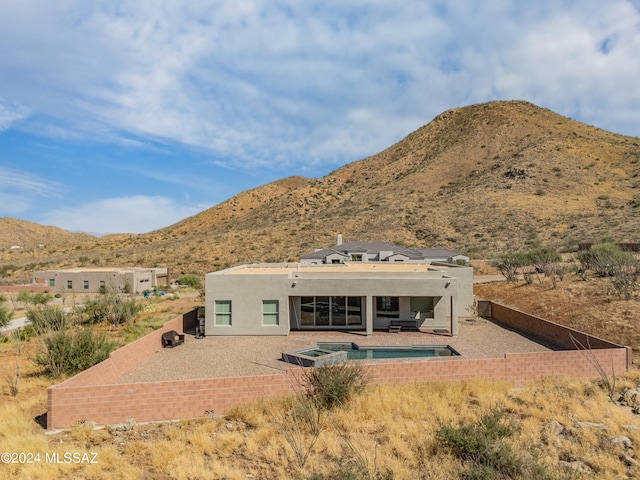 back of property featuring a mountain view, a patio area, and a pool with hot tub