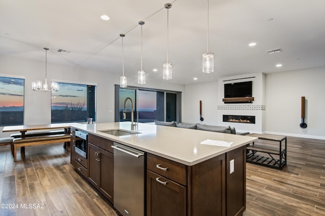 kitchen with dark wood-type flooring, a kitchen island with sink, sink, and hanging light fixtures