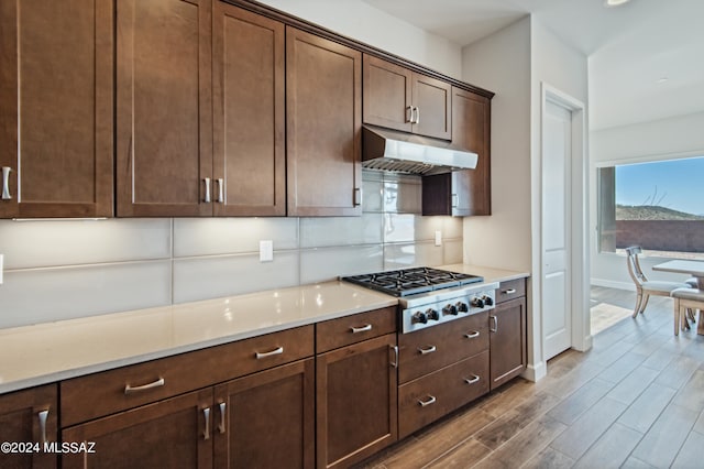 kitchen with stainless steel gas cooktop, hardwood / wood-style floors, dark brown cabinetry, and light stone counters