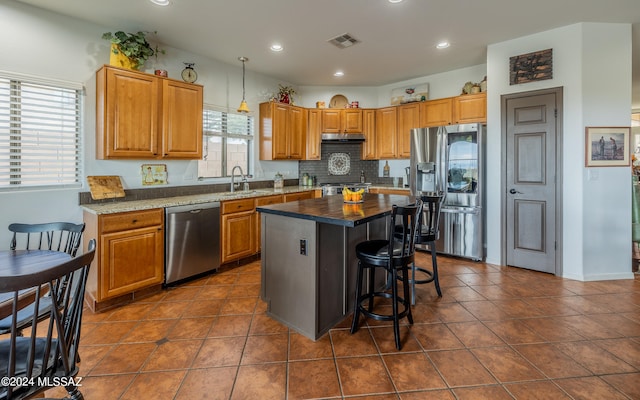 kitchen with a kitchen island, decorative light fixtures, sink, appliances with stainless steel finishes, and a kitchen bar