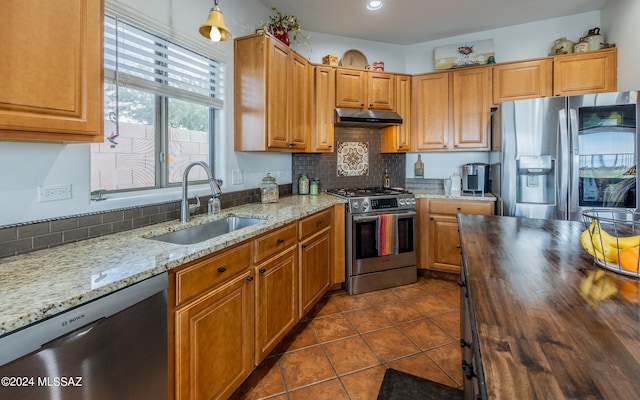 kitchen with tasteful backsplash, butcher block counters, dark tile patterned flooring, sink, and appliances with stainless steel finishes