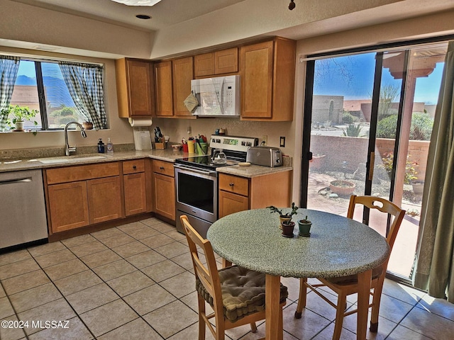 kitchen with a sink, appliances with stainless steel finishes, brown cabinetry, a toaster, and light tile patterned flooring