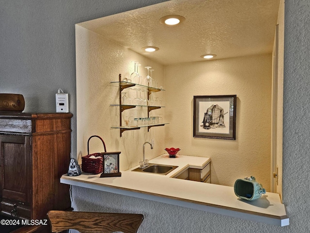 bar with wet bar, a textured ceiling, a textured wall, and a sink