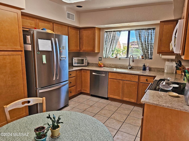 kitchen with light stone counters, light tile patterned floors, appliances with stainless steel finishes, and sink