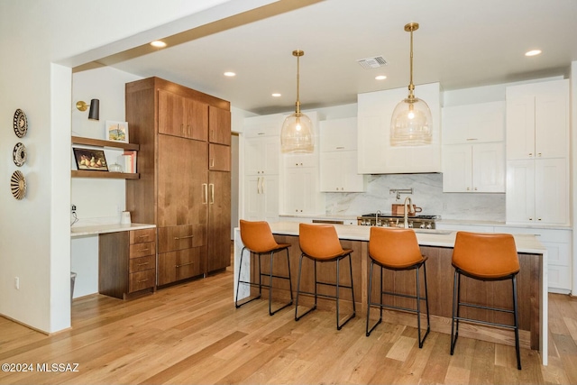 kitchen with a center island with sink, hanging light fixtures, light wood-type flooring, tasteful backsplash, and white cabinetry