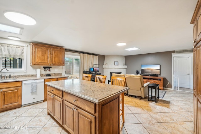 kitchen featuring white dishwasher, a kitchen breakfast bar, sink, light tile patterned floors, and a kitchen island