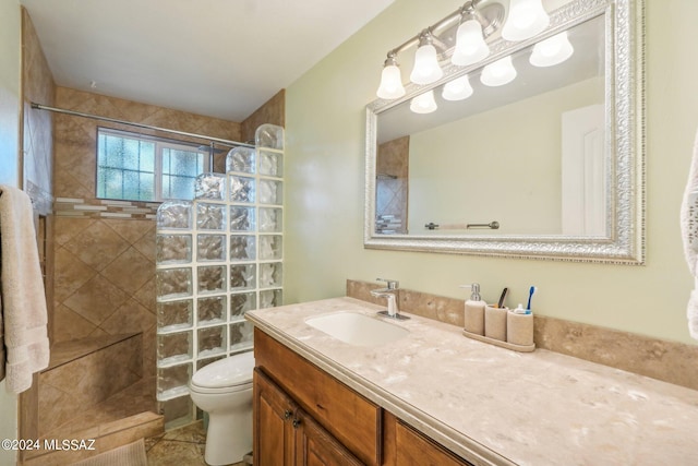 bathroom with a tile shower, tile patterned flooring, vanity, and toilet