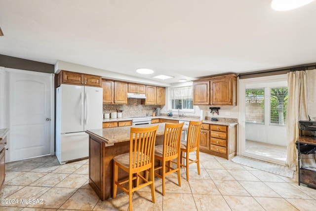 kitchen with sink, a kitchen island, white appliances, a breakfast bar, and light tile patterned floors