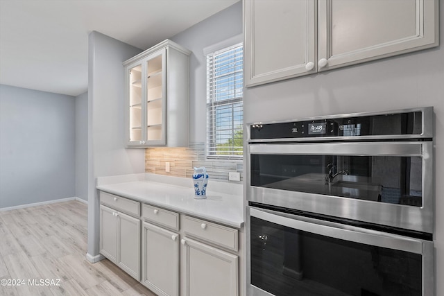 kitchen featuring light hardwood / wood-style floors, double oven, white cabinets, and backsplash