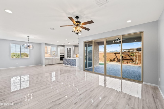 unfurnished living room with ceiling fan with notable chandelier and light hardwood / wood-style flooring