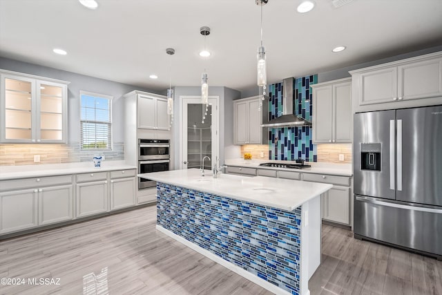 kitchen featuring wall chimney range hood, light hardwood / wood-style floors, pendant lighting, stainless steel appliances, and backsplash